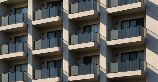 集合住宅のバルコニーが規則的に並ぶ外壁を、早朝の斜光で切り取った建築写真