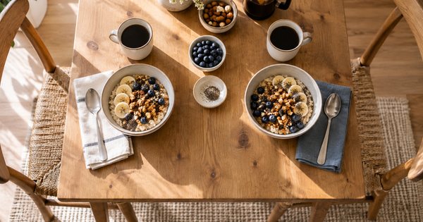 木の食卓に二人分だけ並んだ朝食の器と、窓から差す自然光
